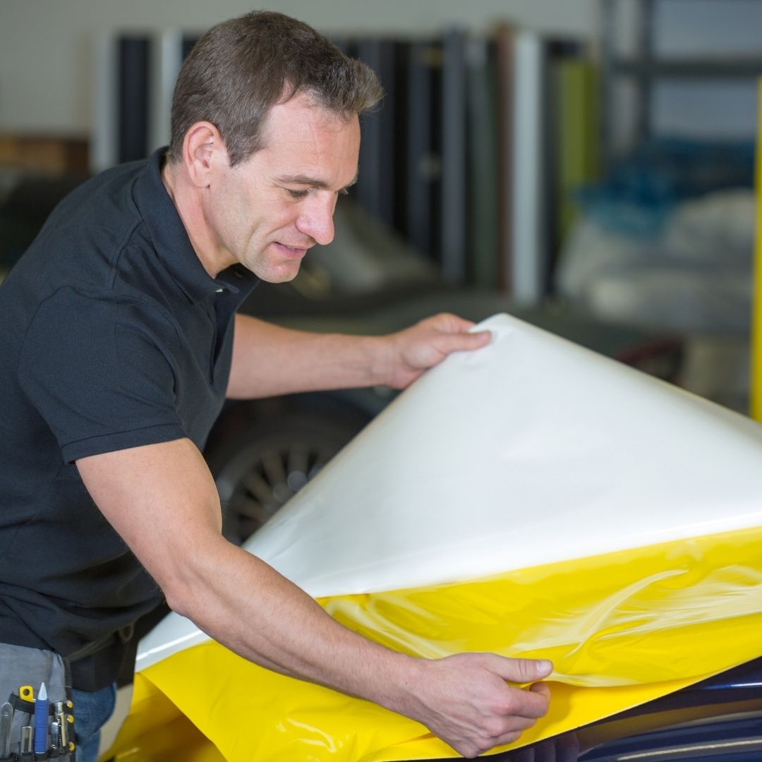 A man applying a vehicle wrap to a car's hood