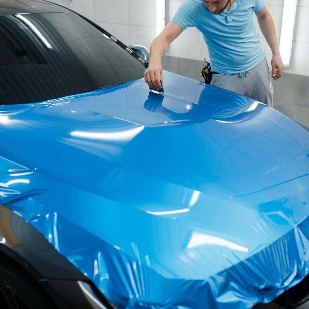 A blue vehicle wrap being applied to a car's hood